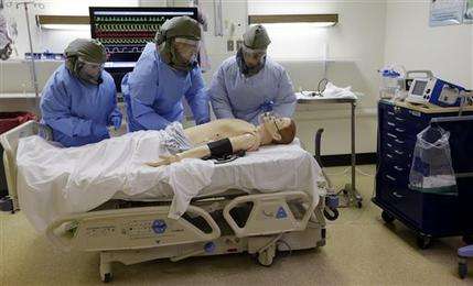 Medical workers wearing protective equipment surround a simulated patient during a demonstration for media members on their training for working with possible Ebola patients, Thursday, Nov. 6, 2014, at Madigan Army Medical Center on Joint Base Lewis McChord, near Tacoma, Wash. Madigan providers and nurses have been training to perform clinical skills, including inserting IVs, obtaining blood samples for testing and conducting ultrasounds while dressed in powered air purifying respirators, impermeable suits and multiple layers of gloves. The clinically-focused exercises use realistic patient simulators that speak through microphones and can express simulated bodily fluids. (AP Photo/Elaine Thompson)