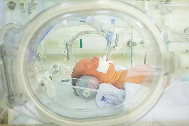 An infant breathes with the help of a respirator in a Neonatal Intensive Care Unit isolette. (Source: UConn)